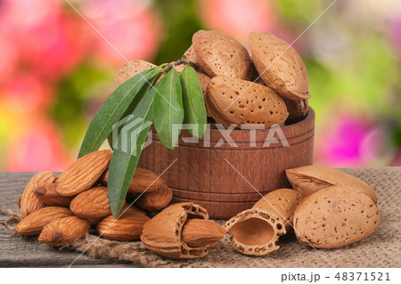 almonds with leaves in a bowl on the old wooden board  blurred garden background 48371521