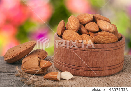 almonds in a bowl on the old wooden board with sackcloth and blurred garden background 48371538