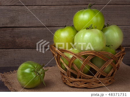 unripe green tomatoes in a wicker basket on wooden table with sacking 48371731