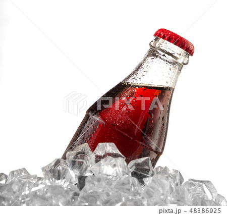 Brown carbonated drink in wet bottle with red cap in ice cubes 48386925