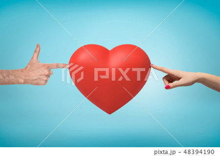 Woman's hand on the right and man's hand doing finger gun on the left touching a big red Valentine 48394190