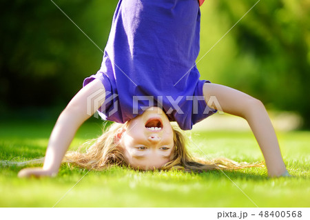 Happy young child playing head over heels on green grass in spring park 48400568