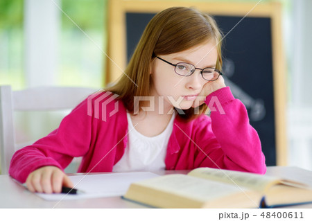Stressed and tired schoolgirl studying with a pile of books on her desk 48400611
