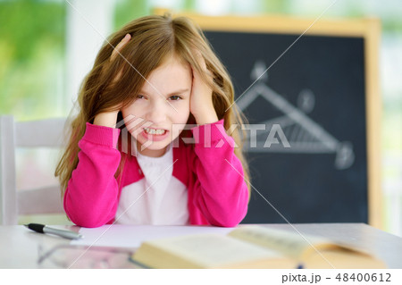 Stressed and tired schoolgirl studying with a pile of books on her desk 48400612