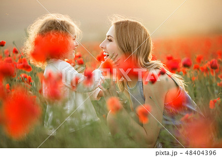 Beautiful smiling child girl with young mother are having fun in field of poppy flowers over sunset Beautiful smiling child girl with young mother are having fun in field of poppy flowers over sunset 48404396