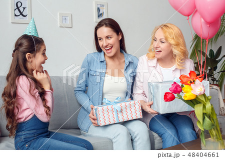 Grandmother mother and daughter together at home birthday sitting girl getting presents surprised Grandmother mother and daughter together at home birthday sitting girl getting presents surprised 48404661