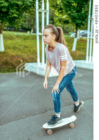 Girl teenager 10-15 years old, riding a skateboard. In the summer in the city in casual jeans and Girl teenager 10-15 years old, riding a skateboard. In the summer in the city in casual jeans and 48407893