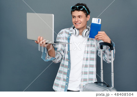 Man isolated on gray wall tourism concept standing with luggage having video call on laptop showing 48408504