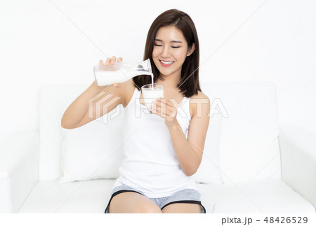 Smiling young Asian woman pours milk in a glass at home. 48426529