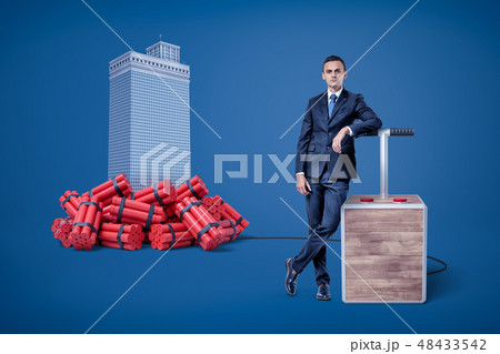 Businessman standing next to detonator box connected to heap of dynamite beside high-rise building Businessman standing next to detonator box connected to heap of dynamite beside high-rise building 48433542