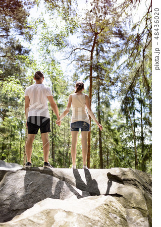 Young couple standing hand in hand on a rock Young couple standing hand in hand on a rock 48436020