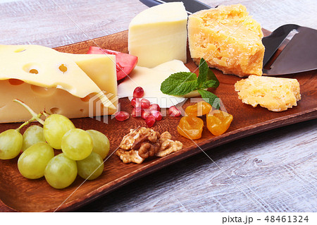 Assortment of cheese with fruits, grapes, nuts and cheese knife on a wooden serving tray. 48461324
