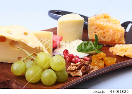 Assortment of cheese with fruits, grapes, nuts and cheese knife on a wooden serving tray. Assortment of cheese with fruits, grapes, nuts and cheese knife on a wooden serving tray. 48461326