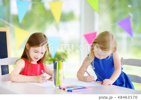 Two cute little sisters drawing with colorful pencils at a daycare Two cute little sisters drawing with colorful pencils at a daycare 48463570