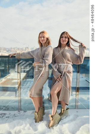 Two women standing in bathrobe on outdoor terrace with winter snowy cityscape 48464096