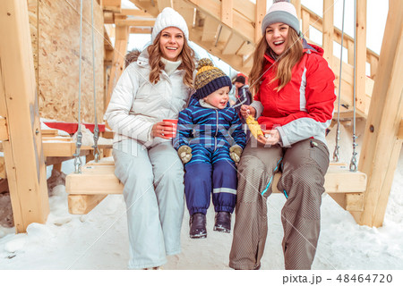 Happy family mom with girlfriend, little son 3-6 years old. Rest in city winter on wooden swing 48464720