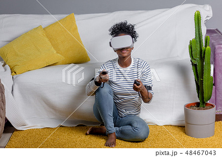 African woman watching video using VR glasses with remote control at home. 48467043