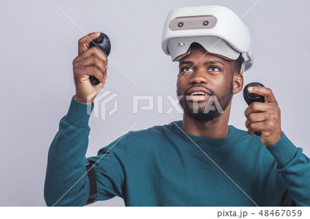 African man wears virtual reality goggles, holds game controllers, isolated 48467059