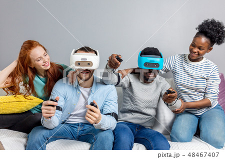 Two guys playing video games using VR glasses and girlfriends support them. 48467407