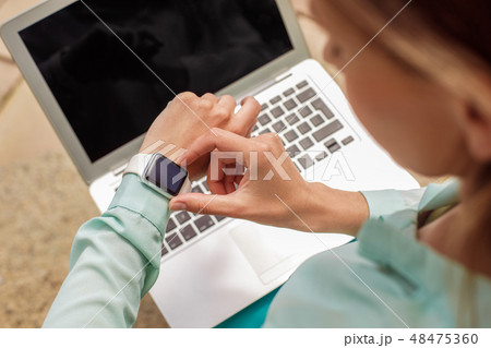 Young woman sitting on stairs working on laptop checking time on watch close-up top view 48475360