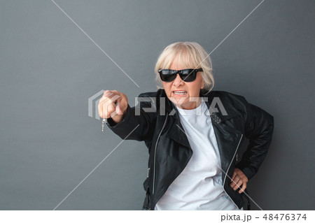 Senior woman in leather jacket and sunglasses studio standing isolated on gray pointing camera Senior woman in leather jacket and sunglasses studio standing isolated on gray pointing camera 48476374
