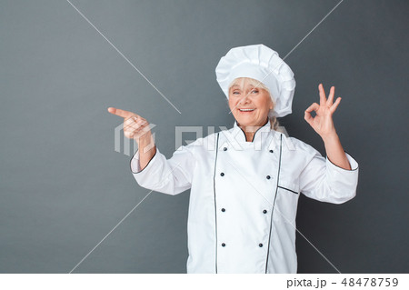 Senior woman chef studio standing isolated on gray showing ok pointing at space asdie happy 48478759