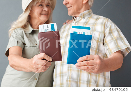 Senior tourists studio standing isolated on gray shwoing passports and tickets close-up blurred Senior tourists studio standing isolated on gray shwoing passports and tickets close-up blurred 48479106