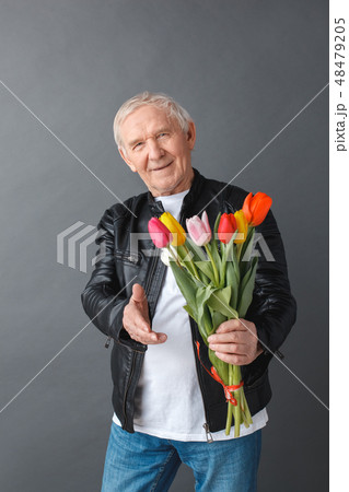 Senior man in leather jacket standing isolated on gray giving bouquet of tulips to camera cheerful 48479205
