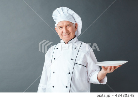 Senior chef studio standing isolated on gray serving plate looking camera joyful 48480248