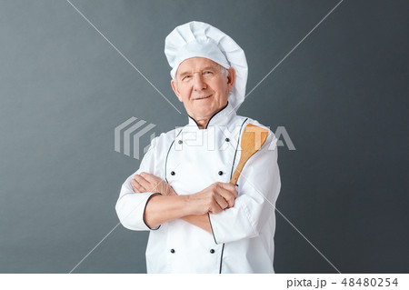 Senior chef studio standing isolated on gray holding spatula crossed arms looking camera proud Senior chef studio standing isolated on gray holding spatula crossed arms looking camera proud 48480254