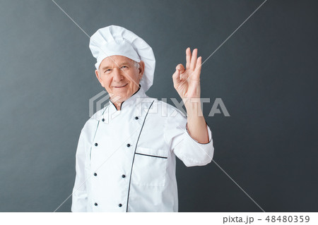 Senior chef studio standing isolated on gray showing ok sign looking camera happy Senior chef studio standing isolated on gray showing ok sign looking camera happy 48480359