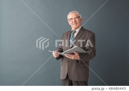 Senior man teacher wearing glasses studio standing isolated on gray holding journal satisfied Senior man teacher wearing glasses studio standing isolated on gray holding journal satisfied 48480443