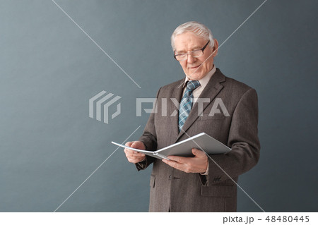 Senior man teacher wearing glasses studio standing isolated on gray reading journal concentrated 48480445