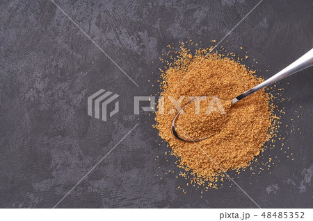 Brown sugar in a metal spoon on a black table 48485352