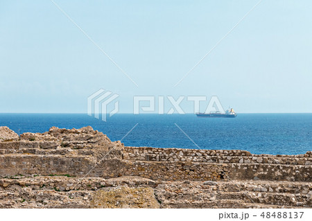 ruins of an ancient amphitheater and a cargo ship sailing in the mediterranean sea 48488137