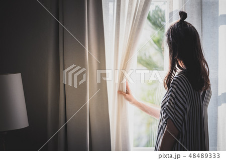 woman opening curtain looking through window 48489333