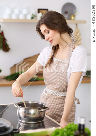 Young brunette woman cooking soup in kitchen. Housewife holding wooden spoon in her hand. Food and Young brunette woman cooking soup in kitchen. Housewife holding wooden spoon in her hand. Food and 48502599