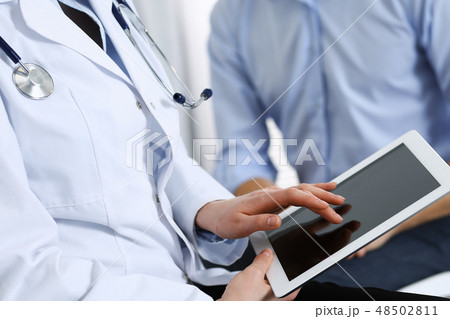 Female doctor using touchpad or tablet computer while consulting man patient in hospital. Medicine 48502811