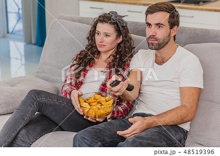 Smiling wife and man sitting on the couch. Watch the TV while eating chips in bed. Smiling wife and man sitting on the couch. Watch the TV while eating chips in bed. 48519396