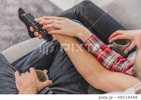 Photo of young happy happy couple sitting on a couch indoors and watching TV. Looking sideways The 48519489