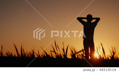 Silhouette A young man enjoys the fresh air and admires the sunset. He holds his hands behind the Silhouette A young man enjoys the fresh air and admires the sunset. He holds his hands behind the 48519519