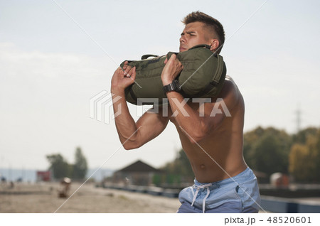 Portrait of handsome man training at the beach with sand bag equipment. 48520601