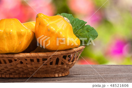yellow pattypan squash with leaf in a wicker basket on wooden table blurred background 48521606