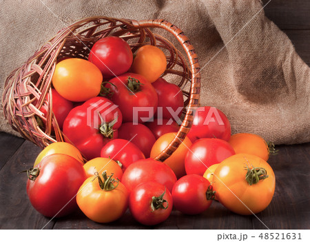 red and yellow tomatoes in a wicker basket on  wooden table 48521631