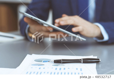 Black pen lying over business analytics papers. Businessman hands using tablet at the background Black pen lying over business analytics papers. Businessman hands using tablet at the background 48532717