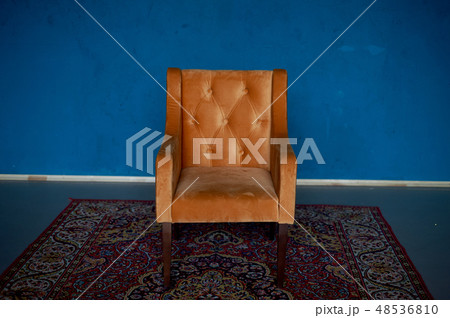 Orange retro armchair with velvet upholstery on a blue wall background.On the floor there is a red Orange retro armchair with velvet upholstery on a blue wall background.On the floor there is a red 48536810
