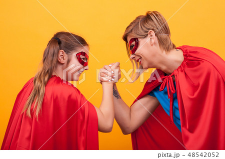 Mother and daughter dressed like superheroes playing arm wrestling over yellow background. Mother and daughter dressed like superheroes playing arm wrestling over yellow background. 48542052