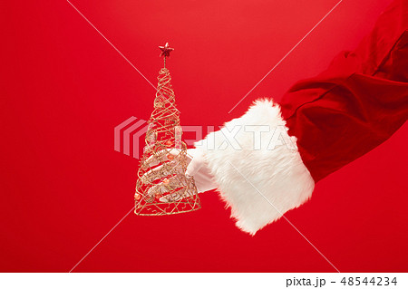 Hand of Santa Claus holding a toy christmas tree on red background Hand of Santa Claus holding a toy christmas tree on red background 48544234