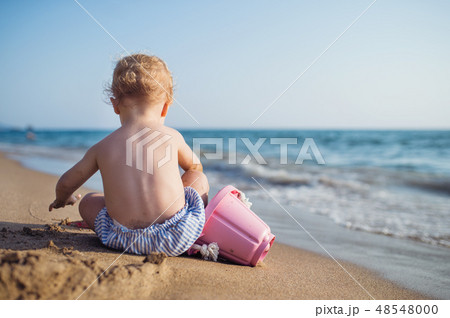 A rear view of small toddler girl sitting on beach on summer holiday, playing. A rear view of small toddler girl sitting on beach on summer holiday, playing. 48548000