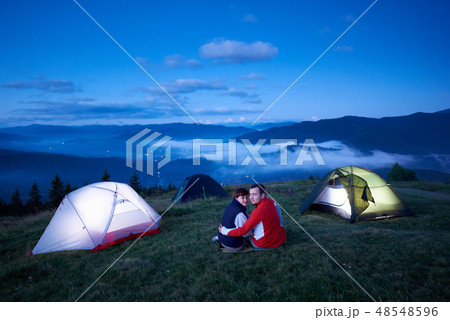 Young couple sitting near tent campus on background of mountain landscape 48548596